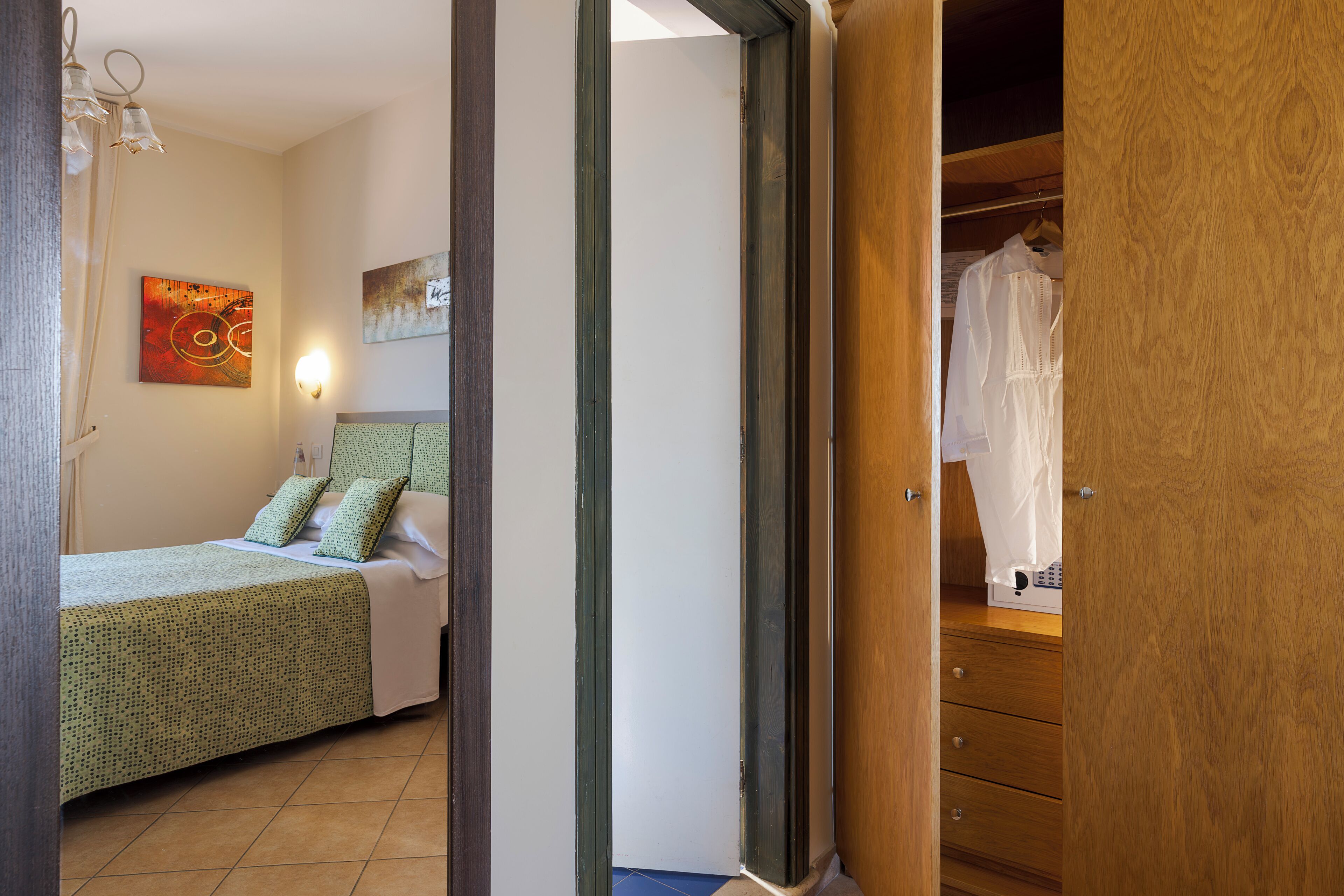 Une chambre à coucher comprenant un lit, une table de chevet, une lampe fixée au mur et une armoire avec des vêtements suspendus.