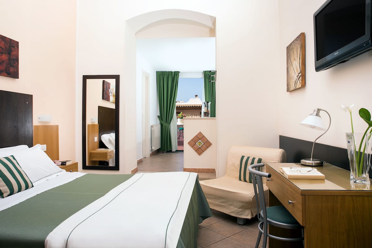 A hotel room with a bed, a desk, a chair, a TV, and a view of the outside.