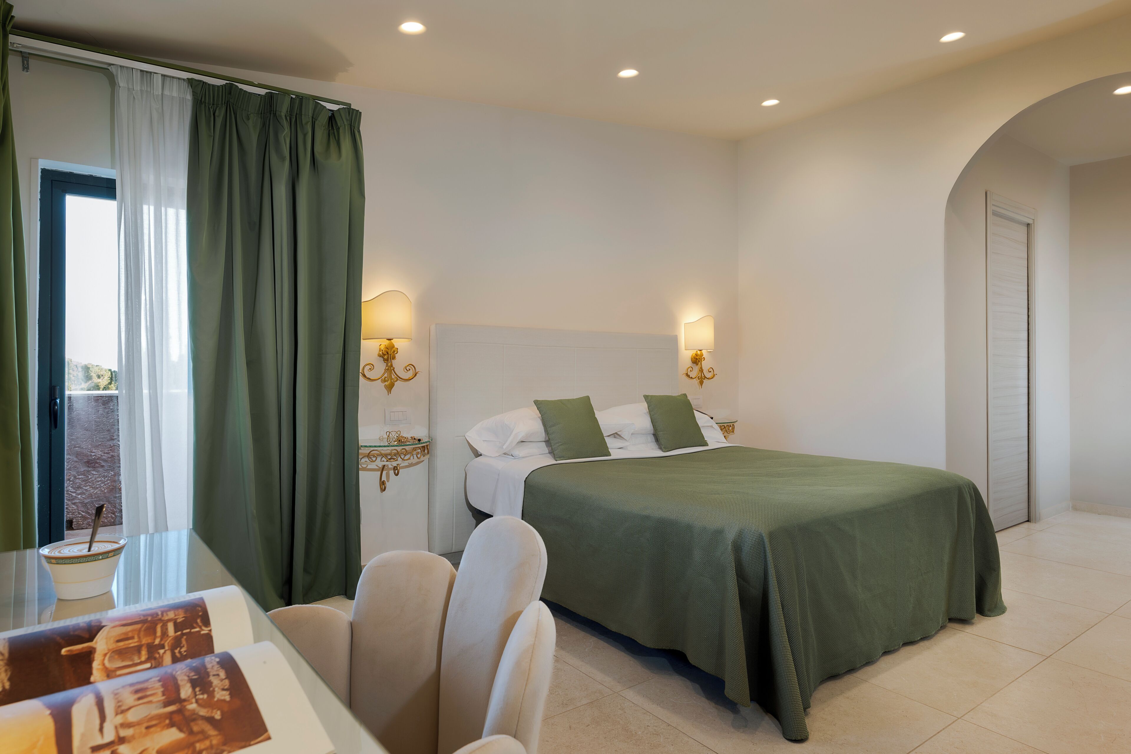 A hotel room with a bed, a table with chairs, a window with curtains, and wall-mounted lamps.