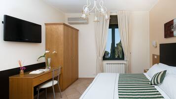 A hotel room with a bed, a desk, a chair, a television, a wardrobe, a window with curtains, and a radiator.
