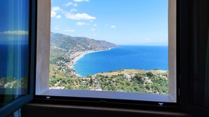 A coastal view through a window, featuring a clear sky, a winding road, and a beach.