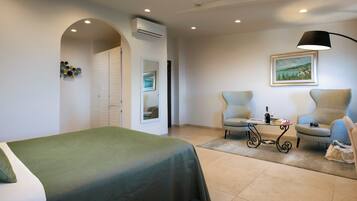 Een hotelkamer met een bed, twee fauteuils, een tafel met lamp, een schilderij aan de muur en een airconditioner.