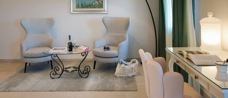 A room with two armchairs, a glass table, a lamp, a desk with a lamp, and a painting on the wall.