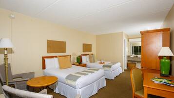 A hotel room with two beds, a desk, a chair, a lamp, and a small table.