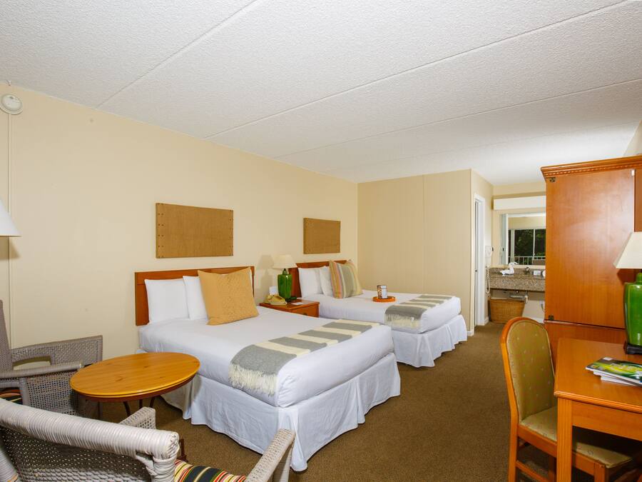 A hotel room with two beds, a desk, a chair, a lamp, and a small table.
