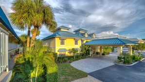 A hotel with a paved driveway, palm trees, and a covered outdoor area with umbrellas. - Naples Garden Inn (Naples)