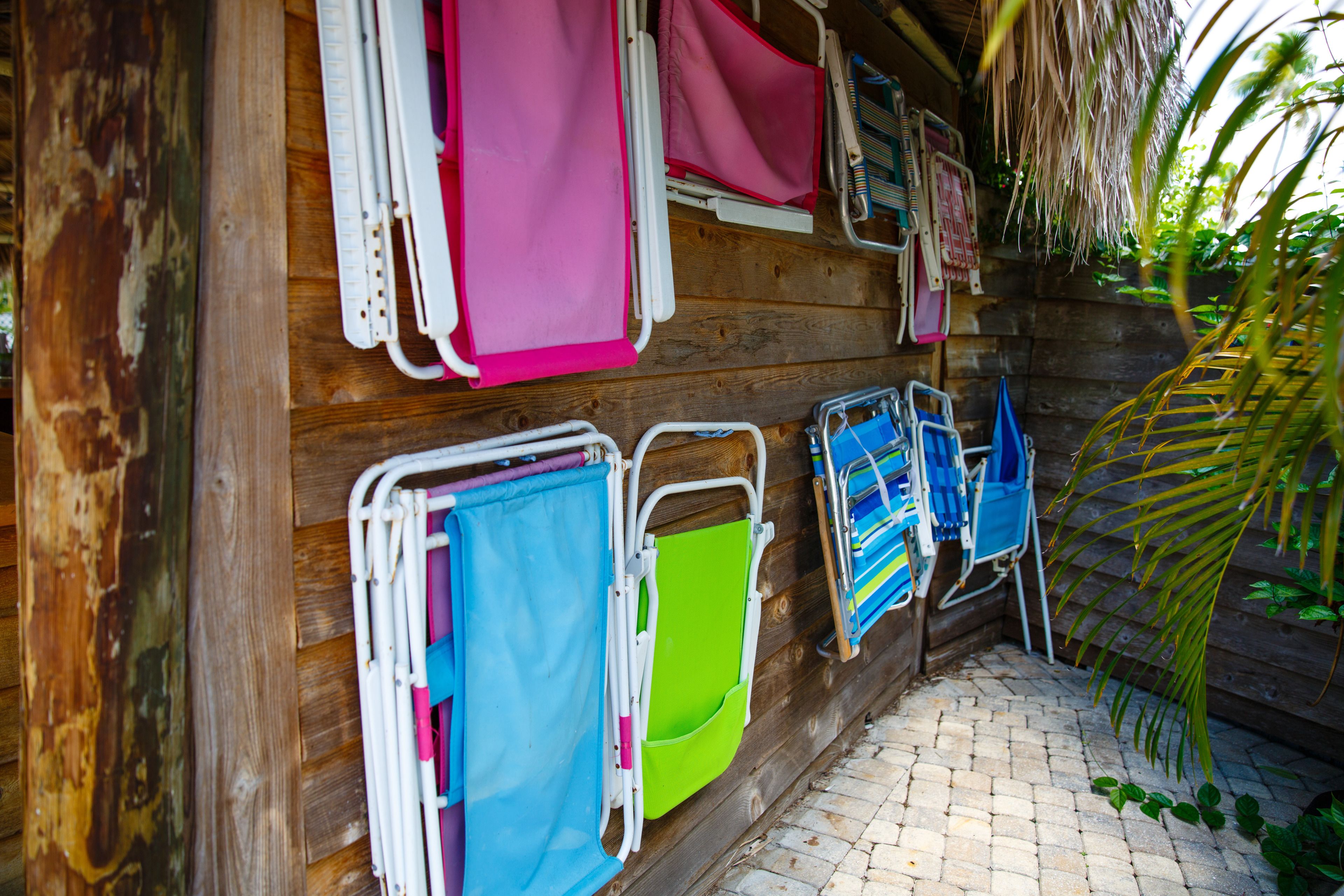 A wooden cabin with a thatched roof, a tiled floor, and several colorful folding chairs and tables neatly arranged against the wall.