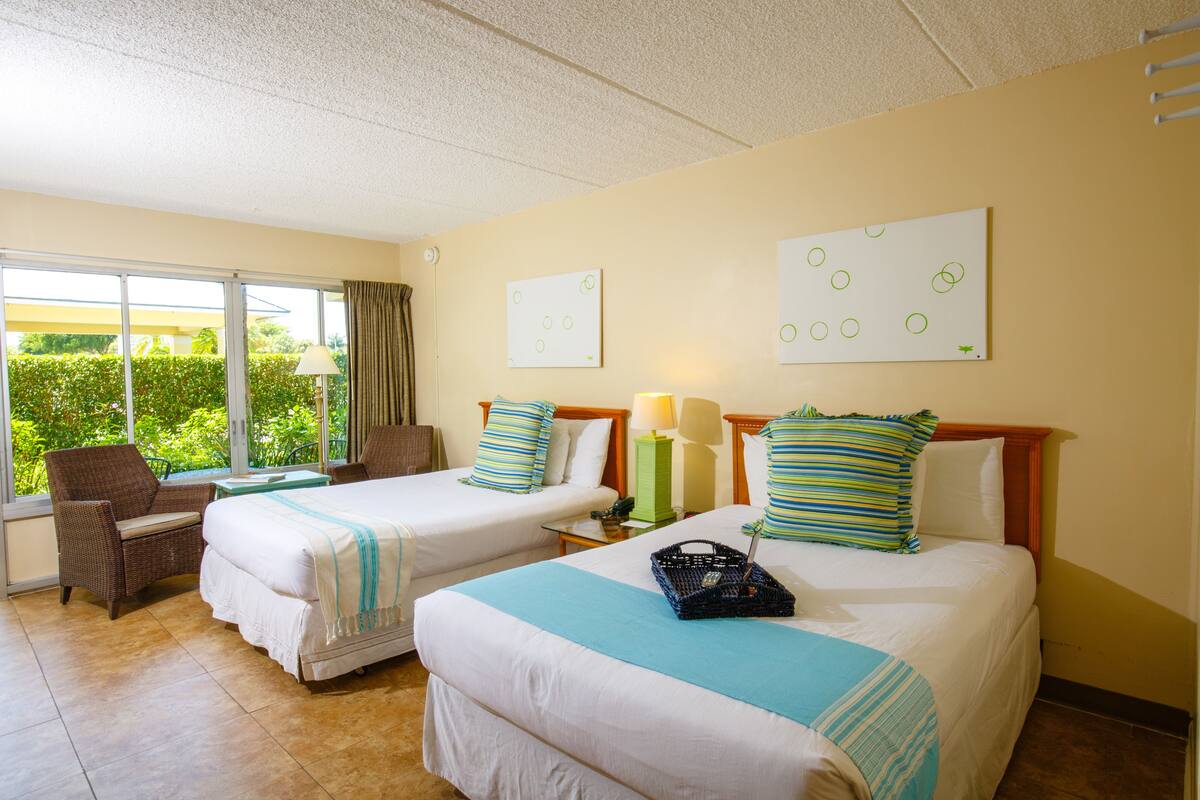 Habitación de hotel con dos camas, una silla, una mesa y ventana con vista a zonas verdes.