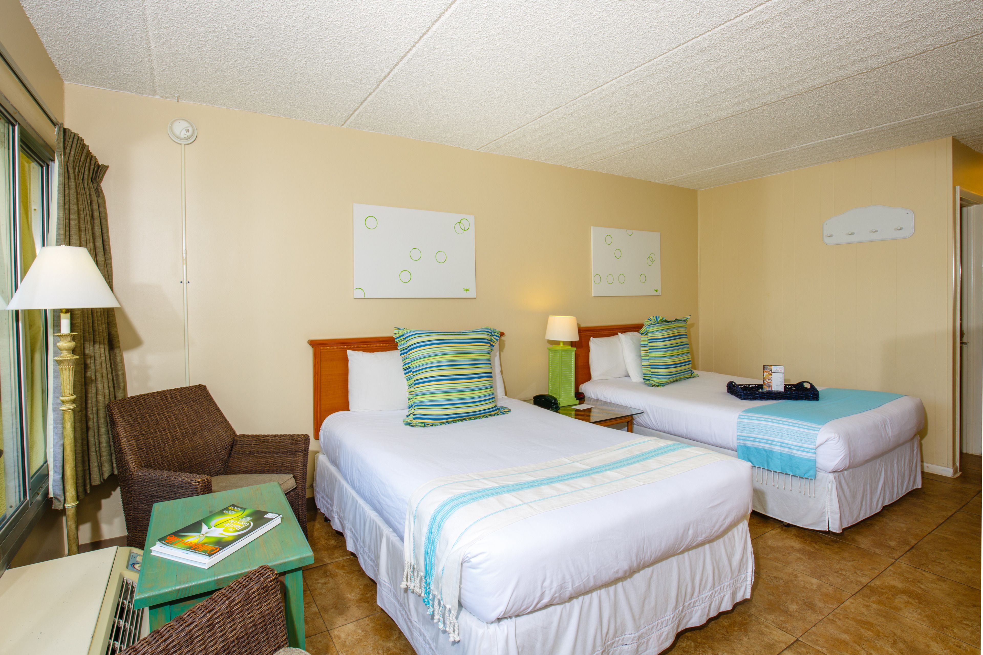 Una habitación de hotel con dos camas, una silla, una mesa y una lámpara.
