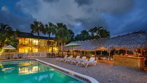 A pool area with lounge chairs and umbrellas, a bar, and a building with a thatched roof. - Naples Garden Inn (Naples)