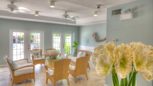 A spacious room with wicker furniture, a dining table, and a large window. - Naples Garden Inn (Naples)