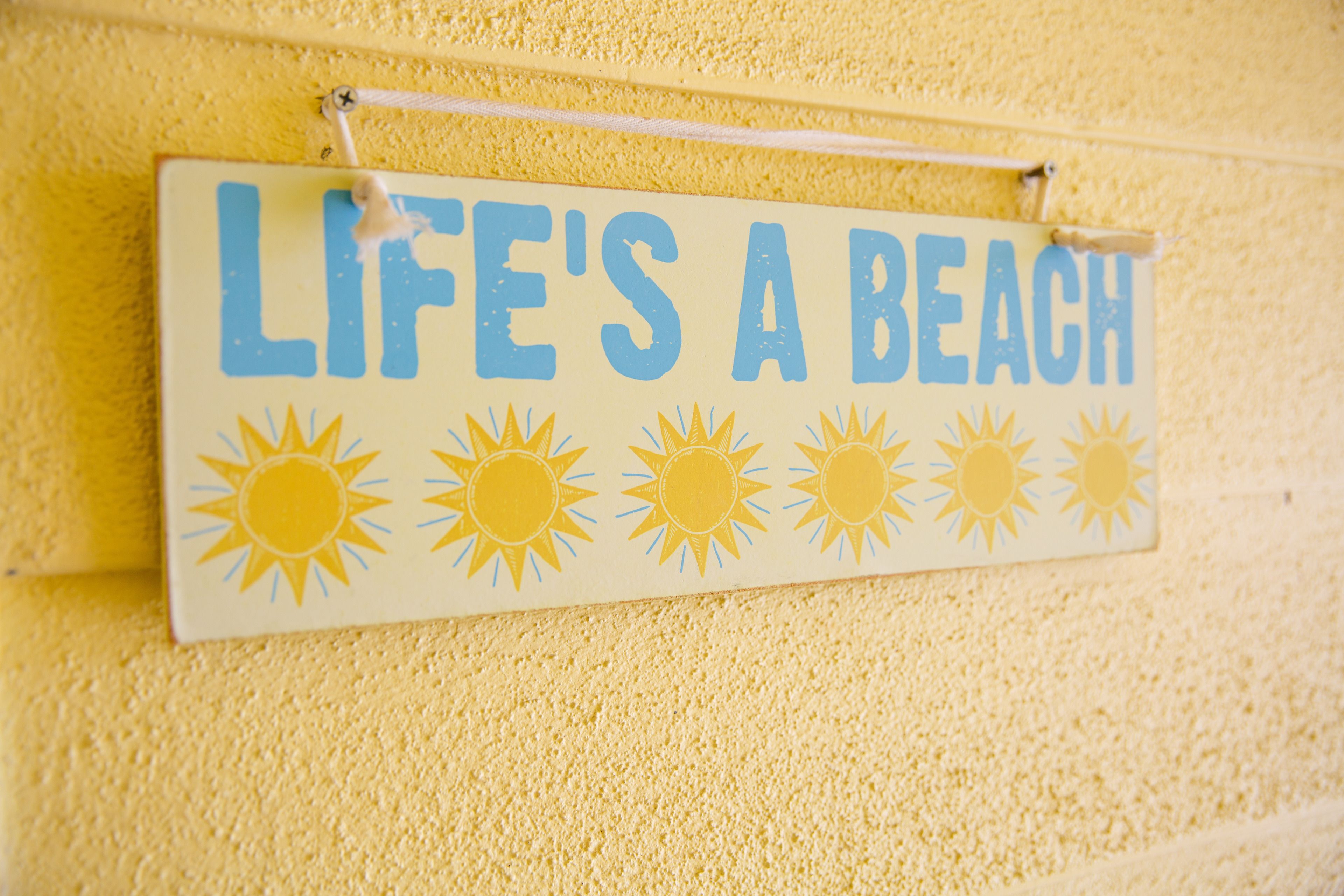 Ein Schild mit dem Text 'LIFE'S A BEACH' und Sonnenillustrationen.