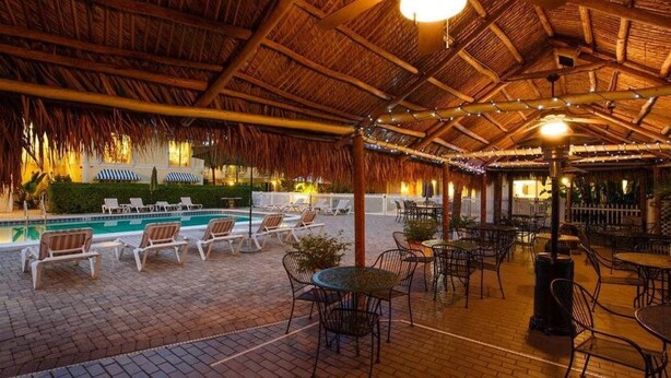 An indoor pool area with lounge chairs and tables, a thatched roof, and string lights. - Naples Garden Inn (Naples)
