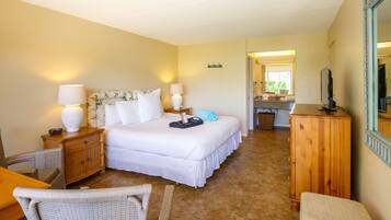 Une chambre d’hôtel comprenant un lit, deux tables de chevet avec des lampes, une commode en bois, une chaise et une petite table.