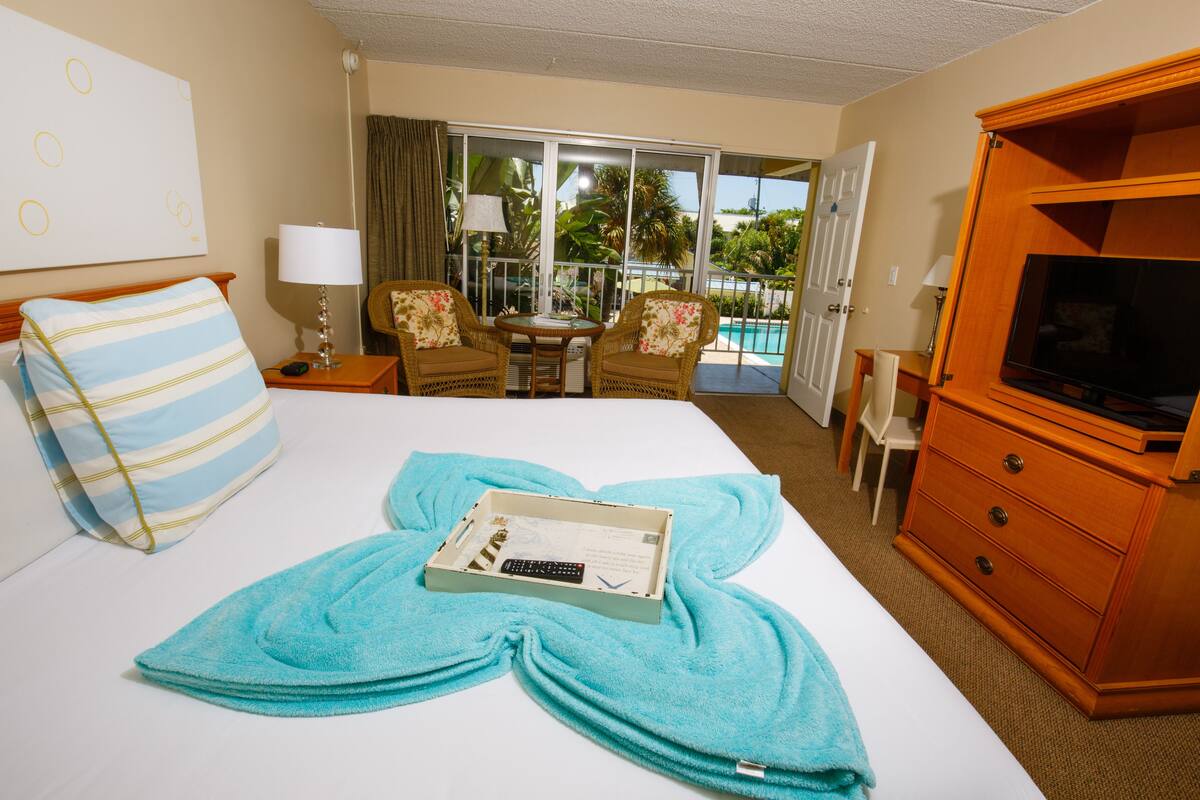 Una habitación de hotel con cama, escritorio con lámpara, silla, televisor y vistas al exterior.
