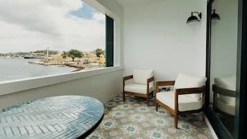 A balcony with two wooden chairs, a round table, and a view of the sea and buildings.