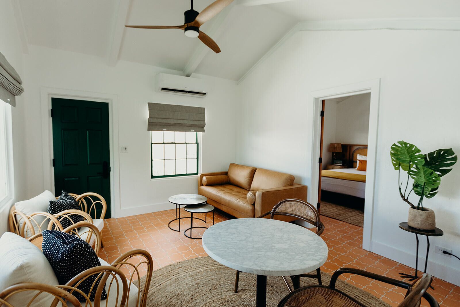 A spacious living area with a brown leather sofa, wicker chairs, a marble table, and a ceiling fan.