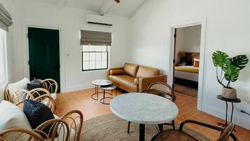 A spacious living area with a brown leather sofa, wicker chairs, a marble table, and a ceiling fan.