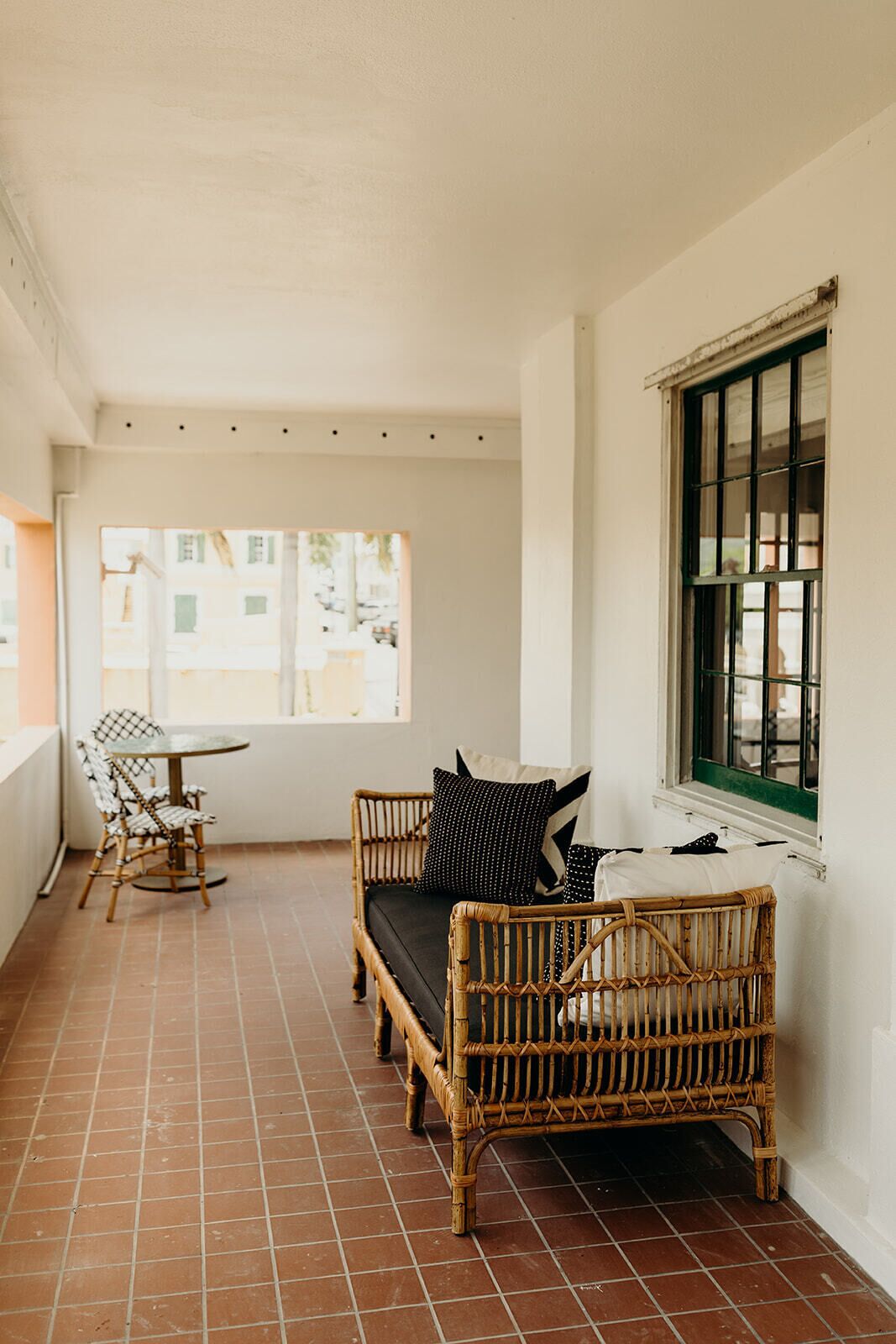A balcony with a wicker sofa, a small table, and chairs. There is a window with green frames.