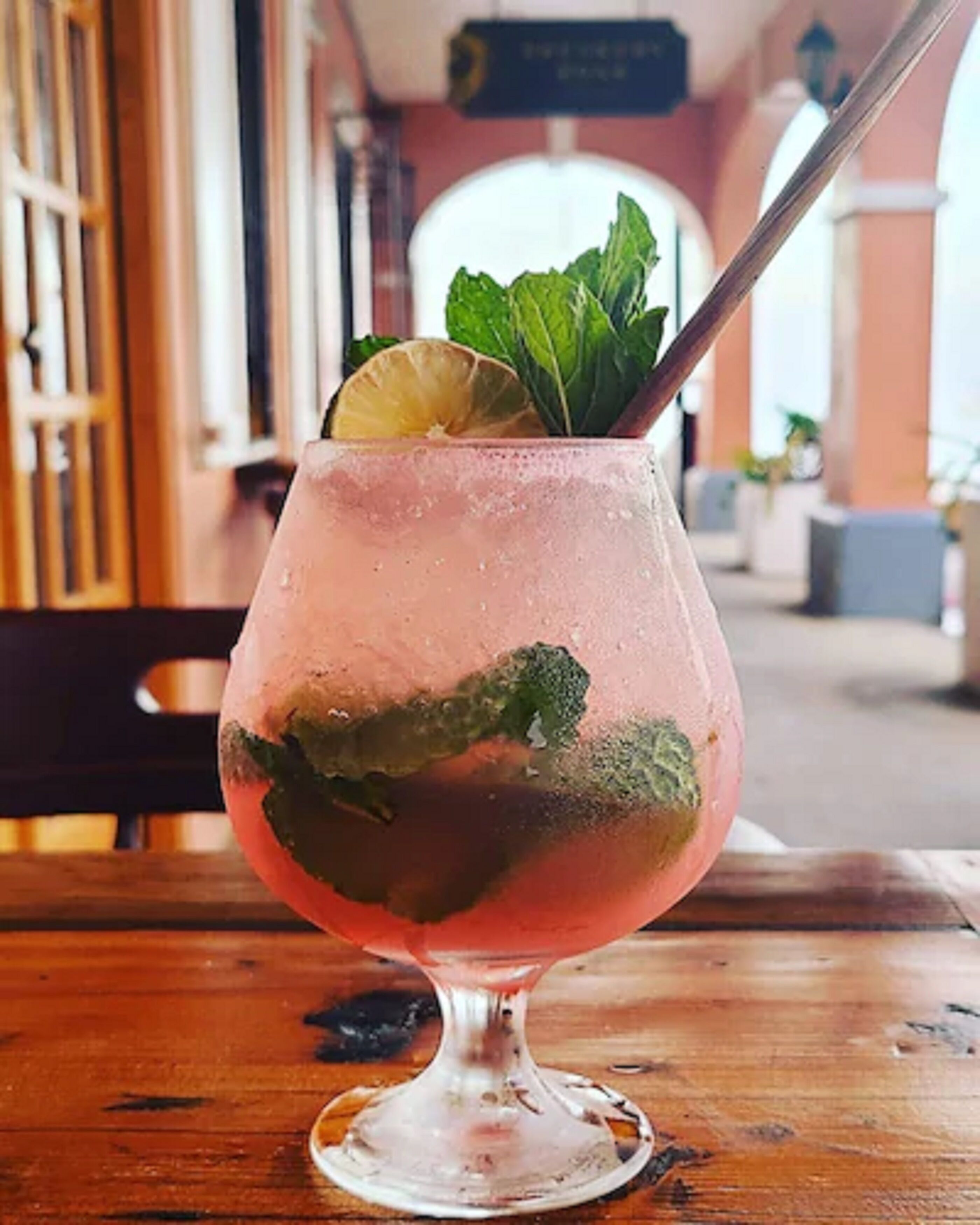 A cocktail glass with a lime wedge and mint leaves on a wooden table.