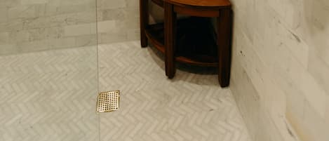 A shower with white marble tiles, a wooden stool, and a towel rack.