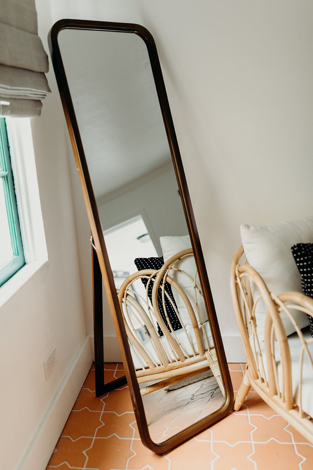 A room with a large mirror, a wicker chair, and a patterned floor.