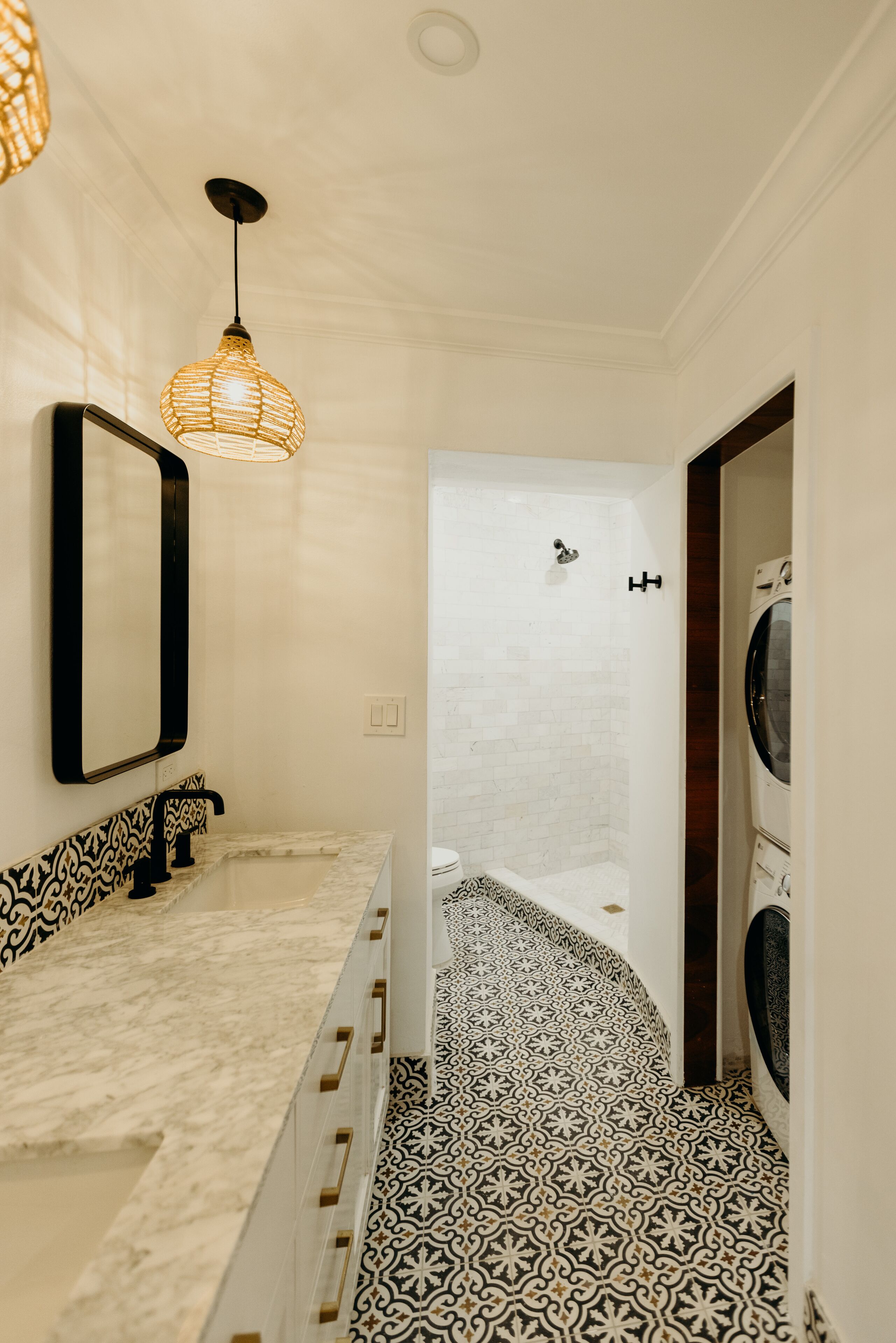 A bathroom with a white and black patterned floor, a marble sink, a hanging light fixture, and a washing machine in the background.