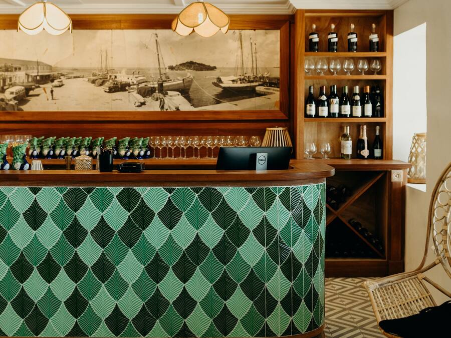 A bar area with a patterned green and black counter, wooden shelves with wine bottles, and a vintage maritime photo above.