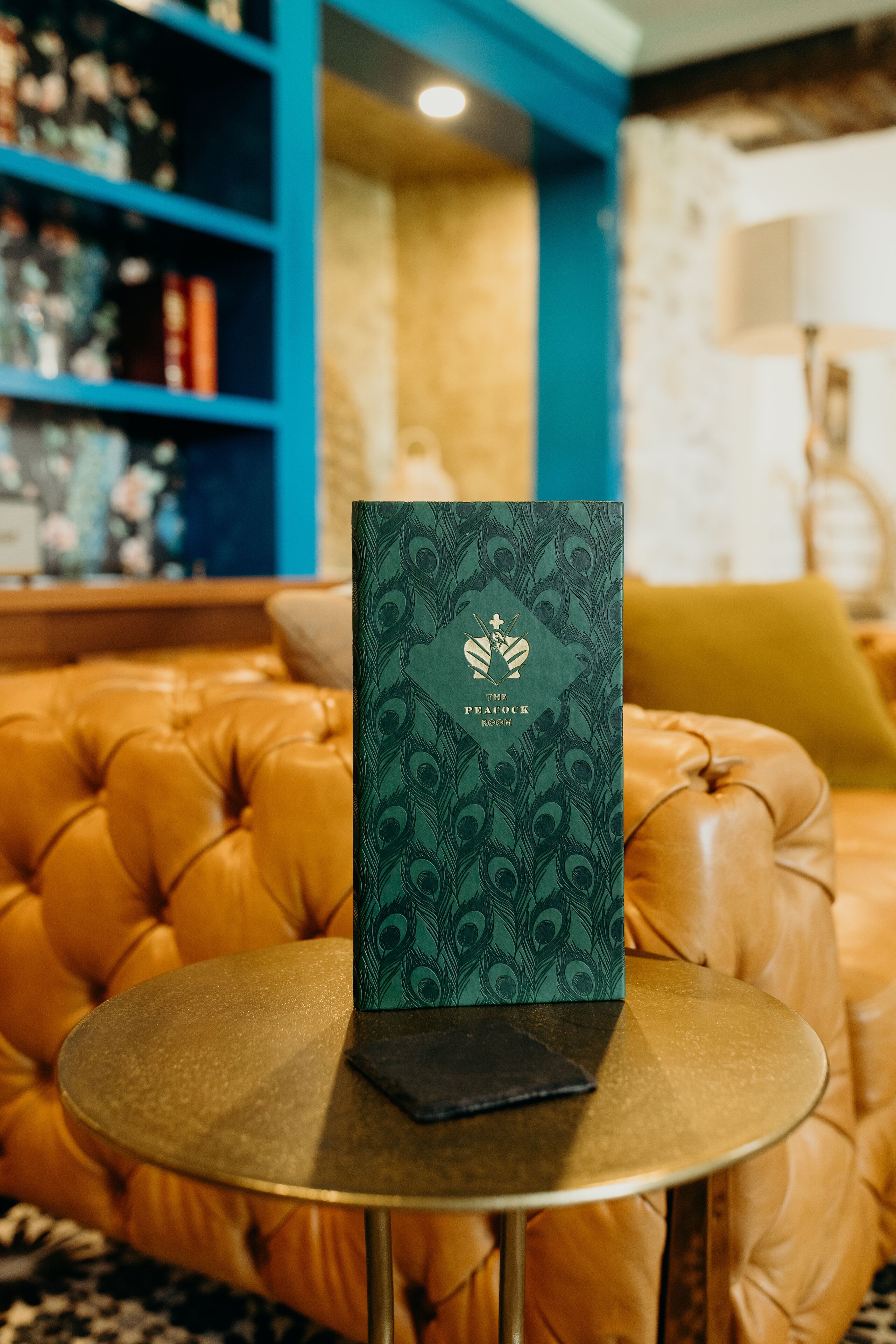 A book titled "The Peacock Room" on a round table with a leather sofa in the background.
