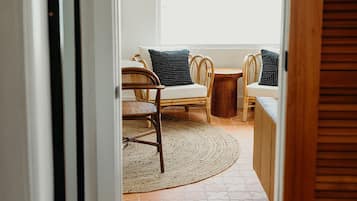 Een gang die uitkomt in een zithoek met rieten stoelen en kussens, een rond tapijt en een raam met uitzicht.