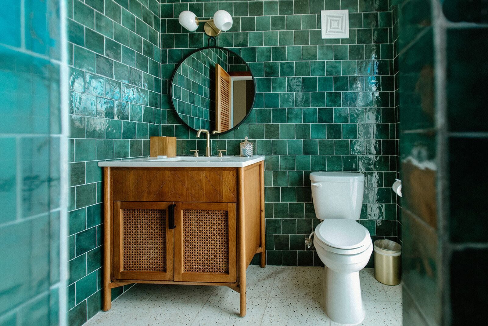 A bathroom with a wooden vanity, a white toilet, and a green tiled wall.