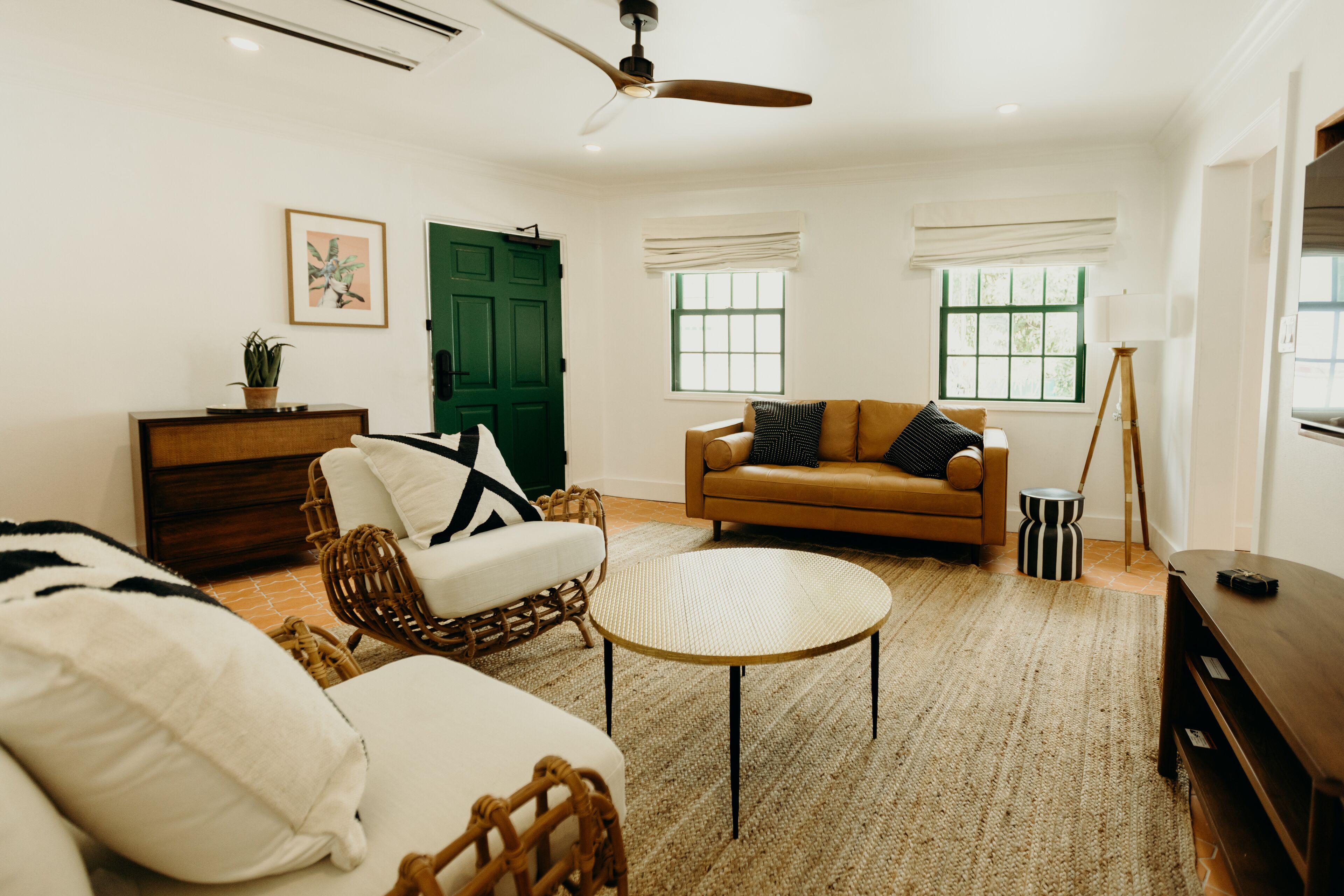 A living room with a sofa, chairs, a round coffee table, a wooden cabinet, and a green door.
