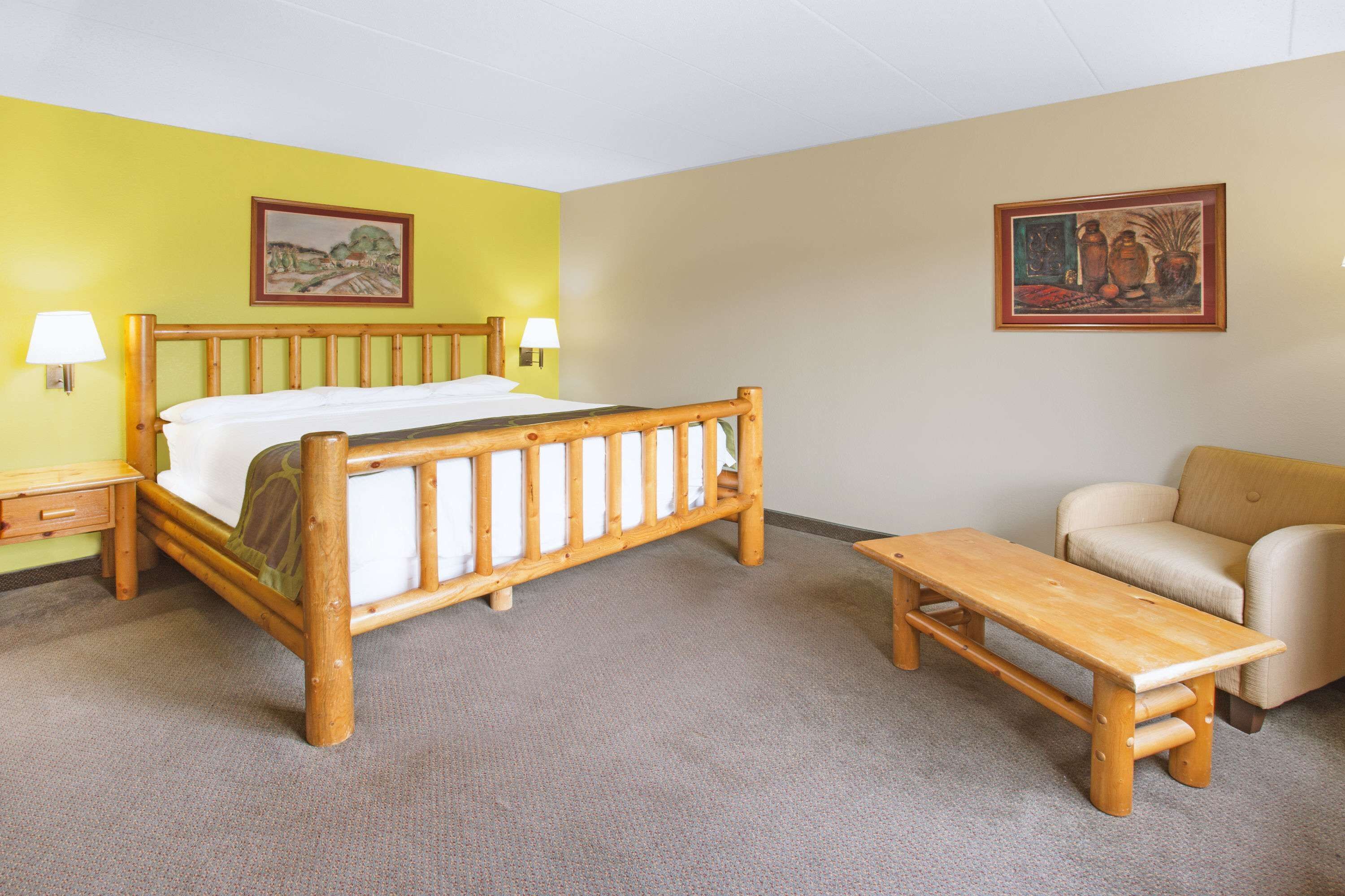 A bedroom with a wooden bed, a wooden bench, a sofa, and two wall-mounted lamps.