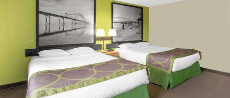 A hotel room with two beds, green bedspreads, a nightstand with a lamp, and two framed pictures on the wall.