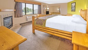Quarto de hotel com cama grande, cabeceira de madeira, escrivaninha, lareira e vista para o exterior.