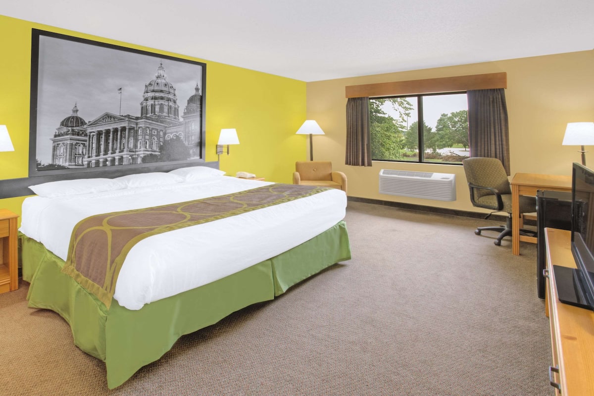 Une chambre d’hôtel avec un grand lit, deux lampes de chevet, un bureau avec un ordinateur, un appareil de climatisation et une fenêtre avec des rideaux.