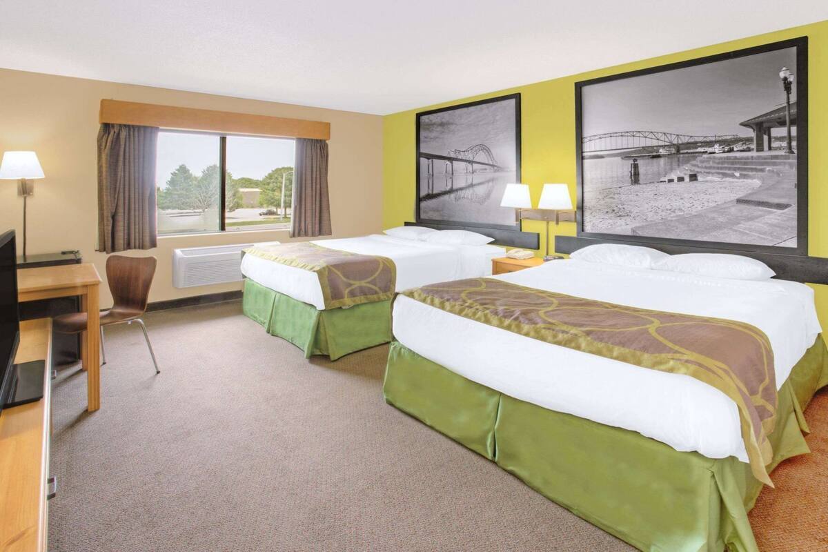 Une chambre d’hôtel avec deux lits, un bureau, une chaise et une grande fenêtre avec des rideaux.