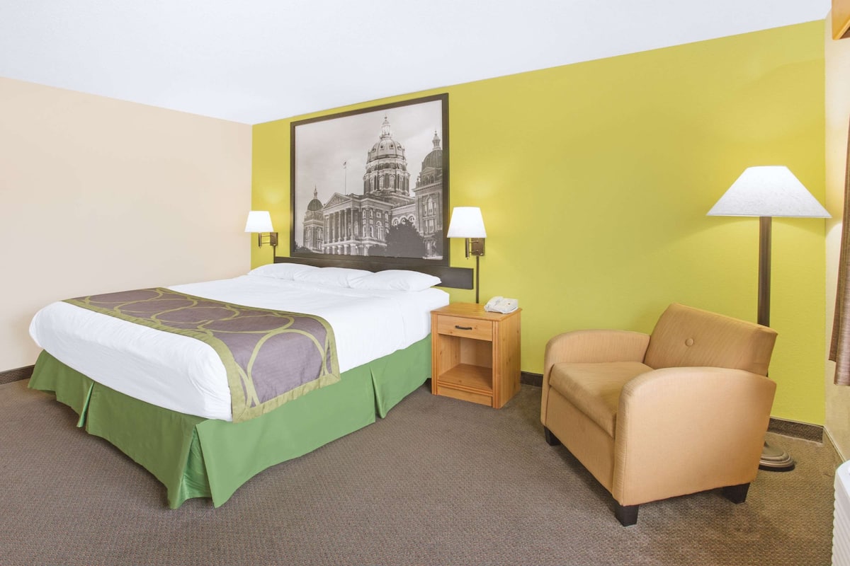 Une chambre d’hôtel comprenant un lit, deux lampes de chevet, une chaise, une table de chevet et une lampe fixée au mur.