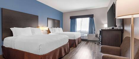 Habitación de hotel con dos camas, un escritorio, una silla, un televisor y una ventana con cortinas.