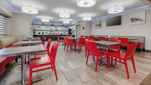 A restaurant with red chairs and tables, a kitchen area, and a TV on the wall. - Best Western Louisville Airport Expo (Louisville)