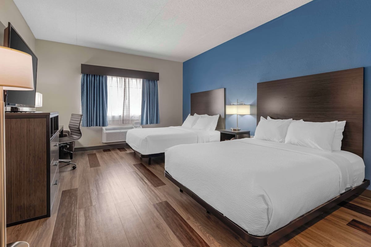 A hotel room with two beds, a desk, a chair, a TV, and a window with curtains.