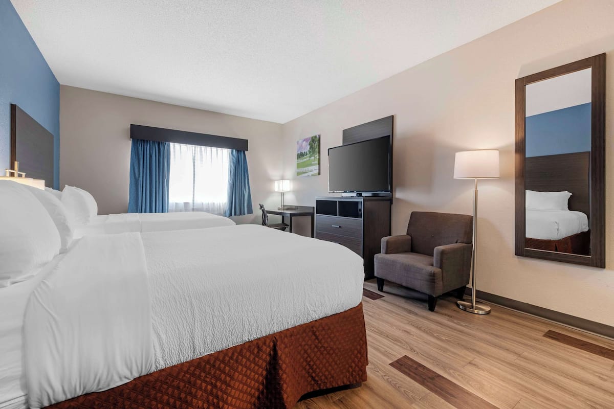 A hotel room with a large bed, a flat-screen TV, a desk, a chair, and a lamp.