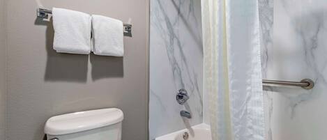 Un baño con inodoro, ducha con puerta de cristal y dos toallas colgadas en un perchero.