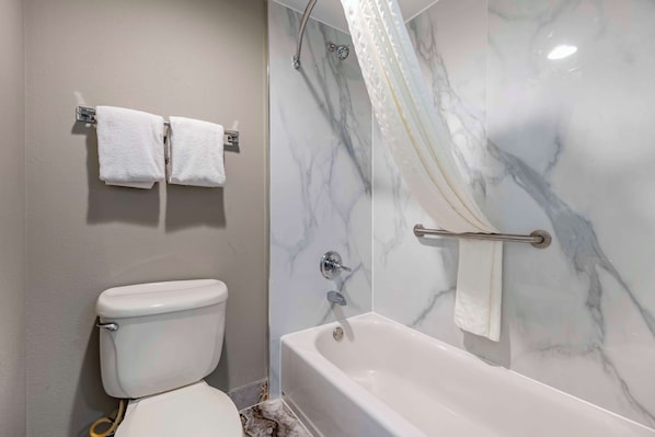Un baño con inodoro, bañera con cortina de ducha y dos toallas colgadas en un perchero.