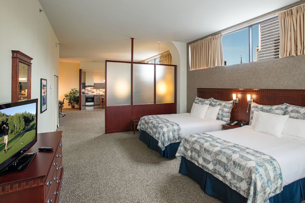 A hotel room with two beds, a TV, a desk, and a view of the city.
