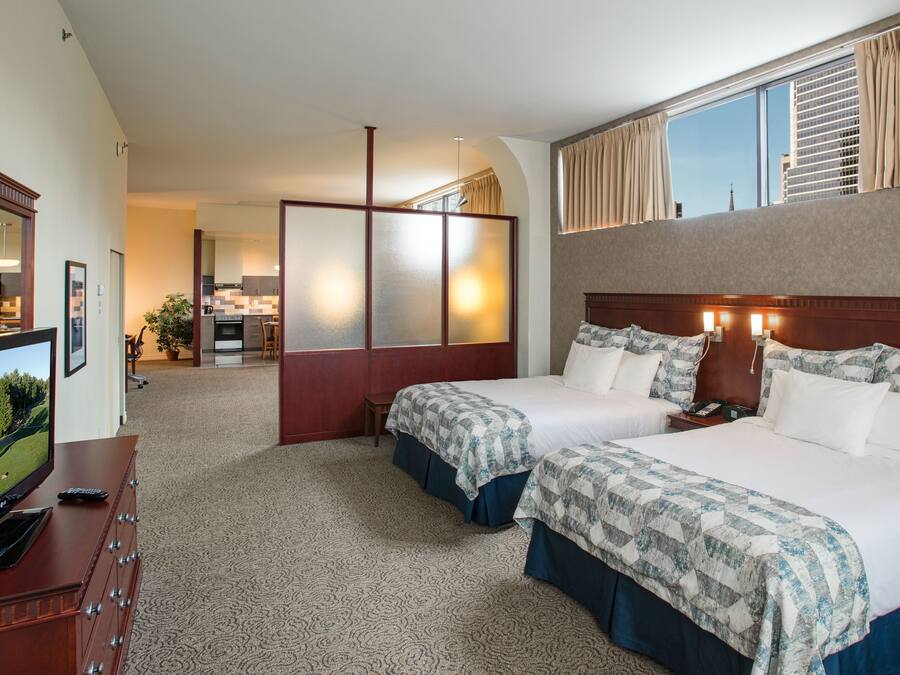 A hotel room with two beds, a TV, a desk, and a view of the city.