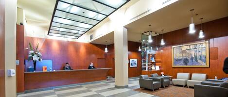 A hotel lobby with a reception desk, seating area, and a large windowed ceiling.