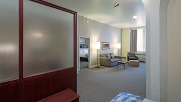 Una habitación de hotel con cama, sofá, sillón, lámpara y ventana con cortinas.