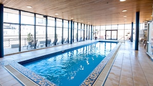 An indoor swimming pool with clear blue water, surrounded by large windows and a tiled floor. - Le Square Phillips Hotel And Suites (Montreal)