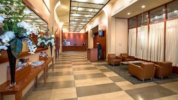 Un vestíbulo de hotel con una recepción, zona de estar y plantas decorativas.
